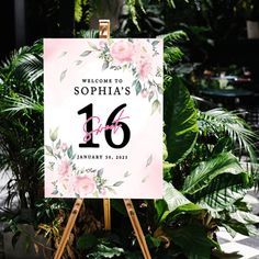 a welcome sign with pink flowers and greenery in the background is displayed on an easel