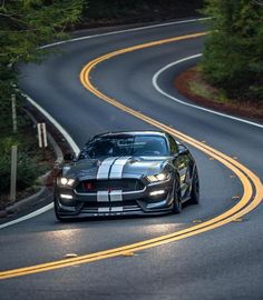 a black and white car driving down a curvy road with trees in the background