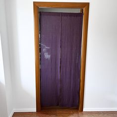 an empty room with a purple curtain in the corner and wood frame on the door