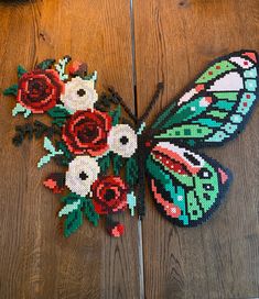 a cross stitch butterfly with flowers on it's wings sitting on a wooden floor