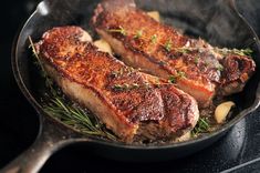 two steaks cooking in a skillet on top of a stove with rosemary sprigs