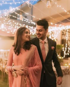 a man and woman standing next to each other in front of string lights on the ceiling