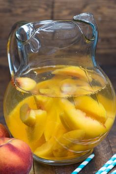 a pitcher filled with liquid next to two peaches