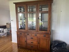 a wooden china cabinet with glass doors in the middle of a wood floored room