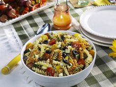 a white bowl filled with pasta and olives on top of a checkered table cloth