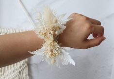 a woman's arm with white and beige flowers attached to it, on top of a wicker table