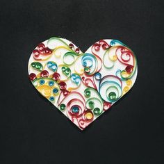 a colorful heart shaped brooch sitting on top of a black surface with lots of different colored buttons