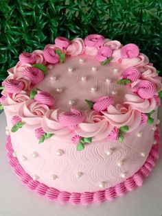 a cake with pink frosting and flowers on it sitting in front of some green grass