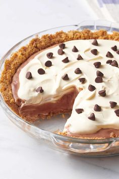 A rich chocolate pudding pie with a graham cracker crust, topped with fluffy whipped cream and scattered chocolate chips, served in a glass pie dish with a slice missing.