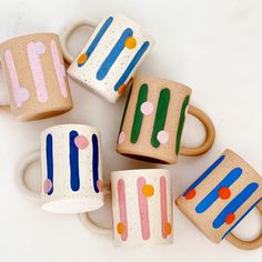 five coffee mugs painted with different colors and shapes on white background, top view