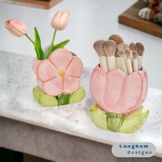 two vases with flowers and brushes in them on a counter top next to each other