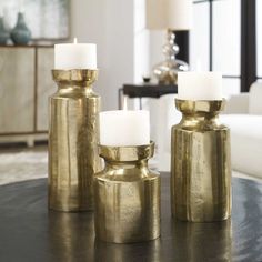 three brass candlesticks sitting on top of a table next to a white couch