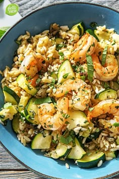 a blue bowl filled with rice, shrimp and zucchini on top of a wooden table