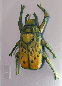 a paper mache of a green and yellow frog hanging on the wall with its legs spread out