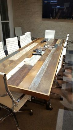 a conference table with white chairs and a flat screen tv on the wall behind it