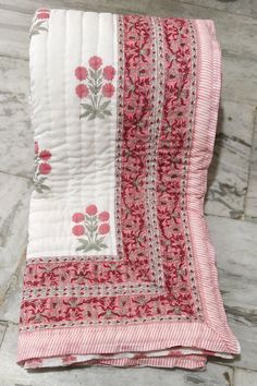 a pink and white quilted blanket with flowers on the bottom, sitting on top of a wooden floor