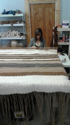 a woman sitting at a table working on an old weaving loom with yarn in the background