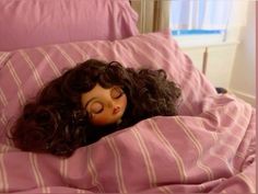 a doll is laying in the bed with her eyes closed