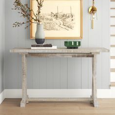 a painting hangs on the wall next to a table with books and flowers in it