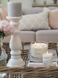 a wicker tray with candles and flowers on it in front of a gray couch