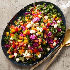 a salad is served in a blue bowl with gold serving utensils on the side