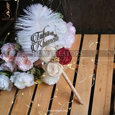 a wedding bouquet with feathers and flowers on a wooden table in front of some string lights