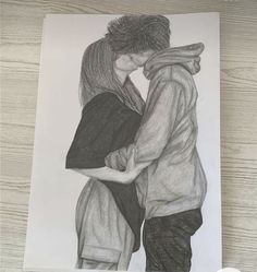 a pencil drawing of two people hugging each other on a table next to a clock