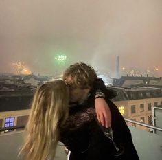 a man and woman kissing on top of a building with fireworks in the sky behind them