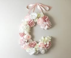 a pink and white flowered wreath hanging on the wall next to a light gray wall