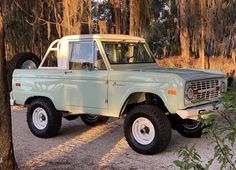 an old pick up truck is parked in the middle of some trees and dirt with two large tires on it