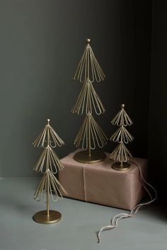 three small gold christmas trees sitting on top of a table next to a wrapped present