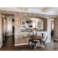 a dining room table and chairs in front of a brick wall with an arched doorway