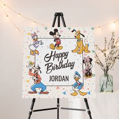 a happy birthday sign with mickey mouse and friends on it in front of a string of lights