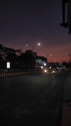 cars driving down the road at night time with street lights and buildings in the background