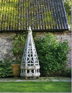 a white sculpture sitting in the middle of a garden next to a building with green roofing