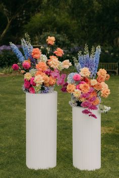 two white vases filled with colorful flowers on top of a grass covered park area