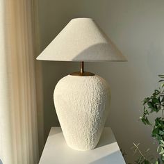 a white lamp sitting on top of a table next to a potted green plant