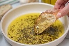 a person dipping some bread into a bowl of oil and olive oil with a spoon