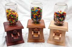 three glass jars with candy in them sitting on wooden stands next to each other against a white background