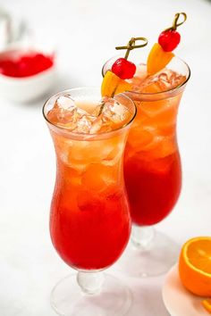 two glasses filled with drinks sitting on top of a table next to an orange slice