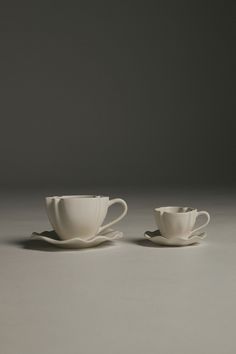 two white cups and saucers sitting on top of a gray countertop next to each other