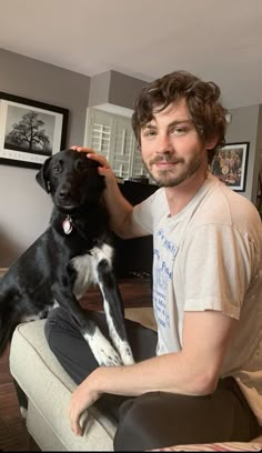 a man sitting on a couch petting a black and white dog