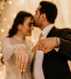 a bride and groom pointing at each other in front of a white backdrop with lights