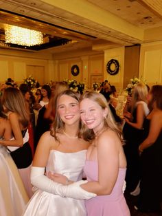 two girls in formal wear standing next to each other at a banquet hall full of people