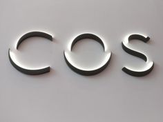 the word cos is illuminated in front of a white wall with black letters on it