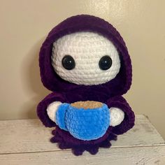 a crocheted stuffed animal with a blue cup in it's hand sitting on a table