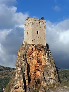 a tall tower sitting on top of a rocky hill under a blue sky with clouds