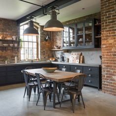 an industrial style kitchen and dining room with exposed brick walls, dark wood cabinets and black chairs