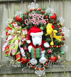 a christmas wreath with a teddy bear and other holiday decorations hanging on a wooden fence