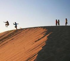 four people standing on top of a sand dune while one person jumps in the air